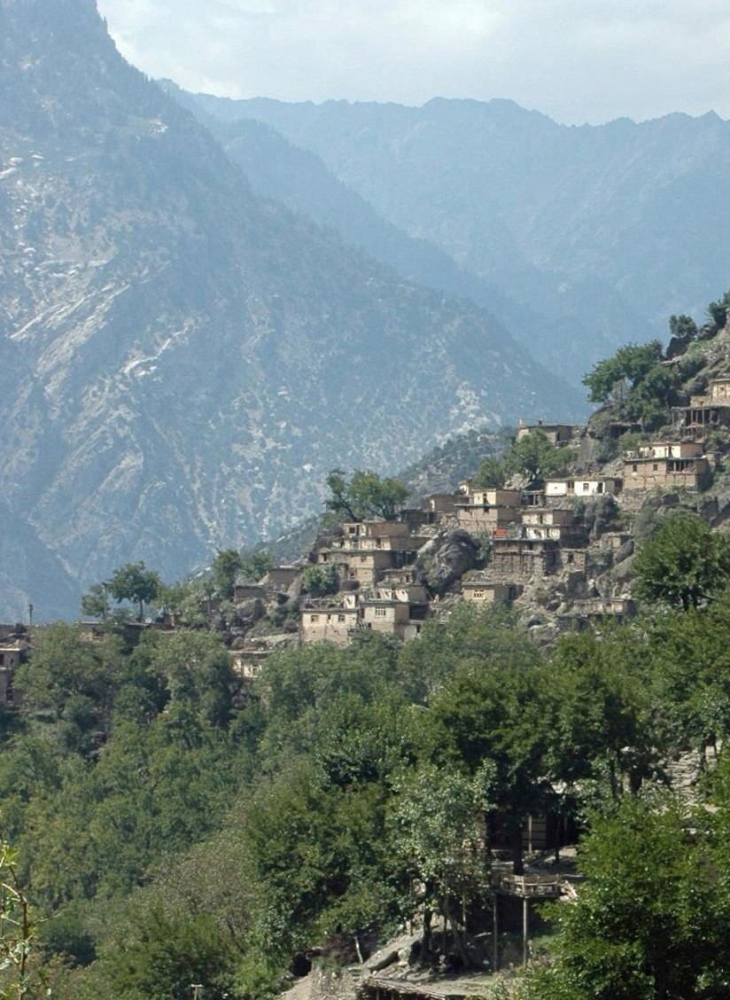 A Nuristan village of stone houses built on a cliff above a forested gorge in the Hindu Kush
